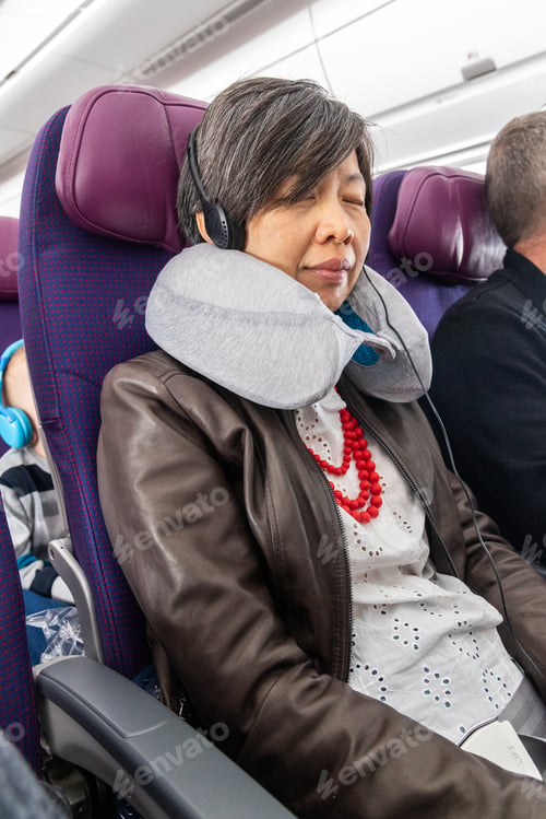 Preview: Asian woman with comfortable neck pillow relaxing during longhaul airplane flight
