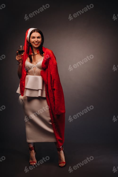Preview: a woman in a Christmas hat and white dress, holding a glass and a red fur coat in her hands, on a