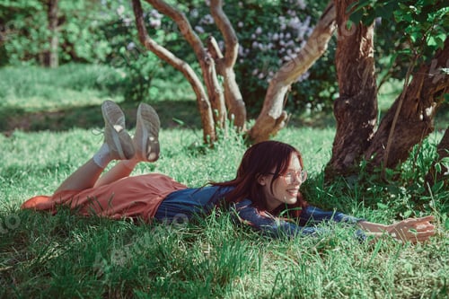 Preview: Teenage girl lying in the grass under a blooming lilac tree, enjoying in a lush garden.
