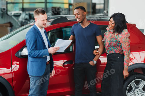 Preview: happy woman receiving a new car from her husband at dealership