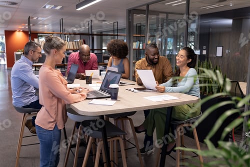 Preview: Multiracial male and female professionals working while using technologies and discussing at table