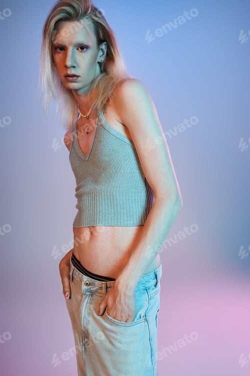 Preview: appealing young non binary person in sexy outfit posing in lights and looking at camera, fashion