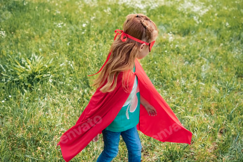 Preview: little child in red superhero costume standing in summer field