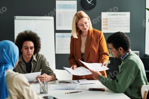 Preview: Happy mature blond teacher passing grammar tests to students