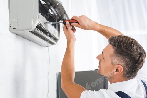 Man Repairing Air Conditioner Unit With Screwdriver