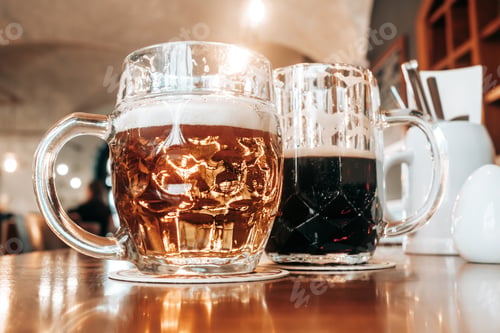 Preview: Two mugs of white and dark beer in pub.