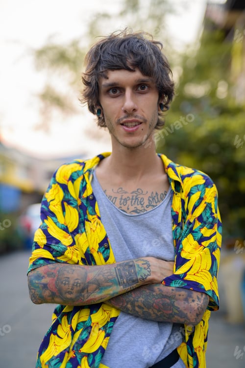 Preview: Portrait of happy young rebellious man smiling with arms crossed outdoors