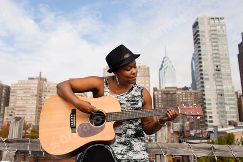 Preview: Mature woman playing guitar in front of Philadelphia skyline, USA