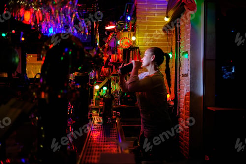 Preview: Female bartender preparing a cocktail with a shaker while working in a bar or pub.