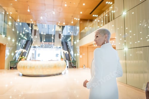 Preview: mature and trendy businesswoman standing in spacious lobby of luxury hotel
