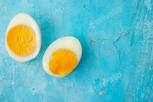 Preview: close-up view of hard-boiled egg cut in half on left side and blue background with copy space