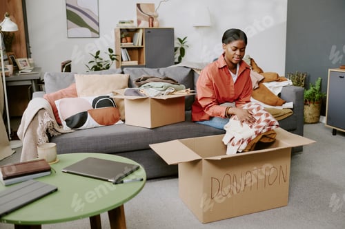 Preview: Black Adult Woman Sorting Clothes for Donation during Home Decluttering