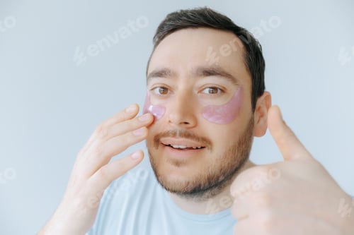 Preview: Man applying eye patches for skincare in a bright indoor setting