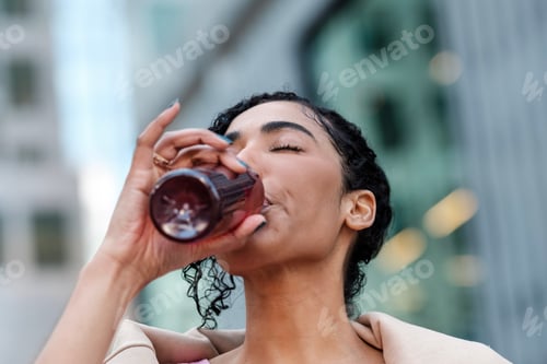 Preview: Headshot of young fitness woman drinking energy drink outdoors.