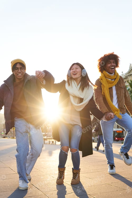Preview: Group of multiracial friends having fun outdoors, walking holding hands and laughing at the city.