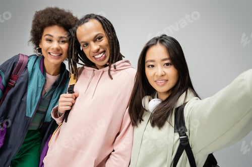 Preview: joyful multicultural students in hoodies and jacket posing and looking at camera isolated on grey