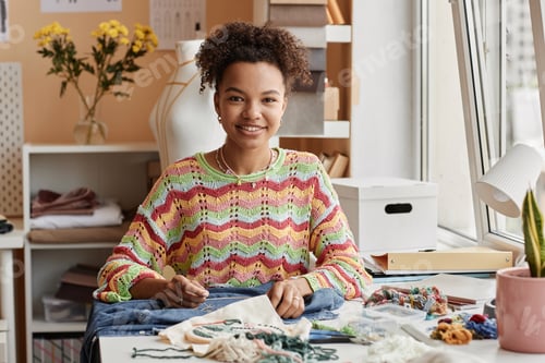 Preview: Happy young African American craftswoman looking at camera with smile while sitting by workplace