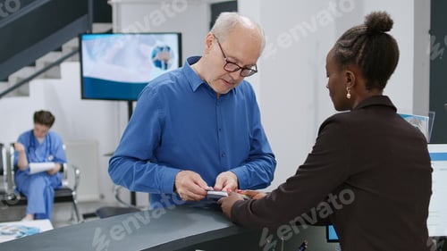 Preview: Senior man paying with credit card at hospital reception desk