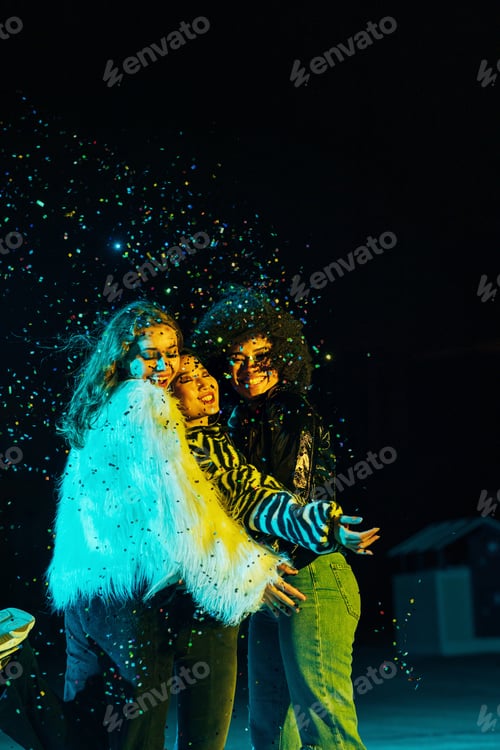 Preview: Three happy female friends embracing each other while standing under confetti at night