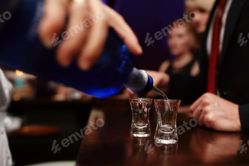 Preview: Bartender pouring strong alcoholic drink into small glasses on bar, shots in a nightclub or bar