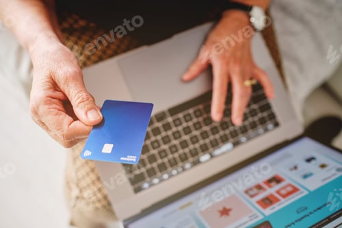 Preview: Woman holding a blue credit card with her hand in front of the computer about to pay for a purchase