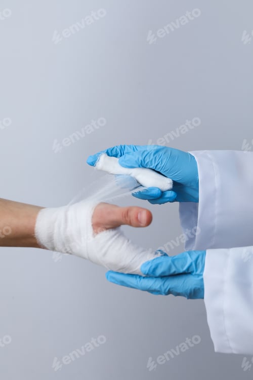 Preview: Concept of help during an injury, doctor wrapping hand in bandage on white background