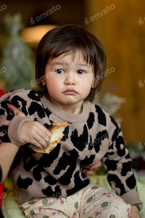 Preview: Little asian girl sitting on a high chair and eating pizza