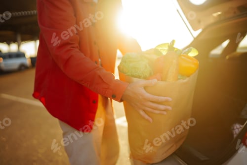 Preview: Young man with shopping bag full of vegetables near the car. Healthy lifestyle.