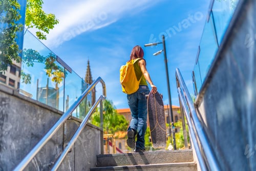 Preview: Rear view of a woman with skateboard walking up stairs