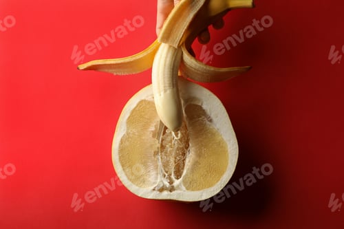Preview: Female hand hold banana with condensed milk on pomelo fruit on red background