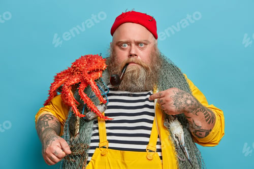 Preview: Photo of serious strict bearded mariner works on sailboat, points at himself and asks who me, has th