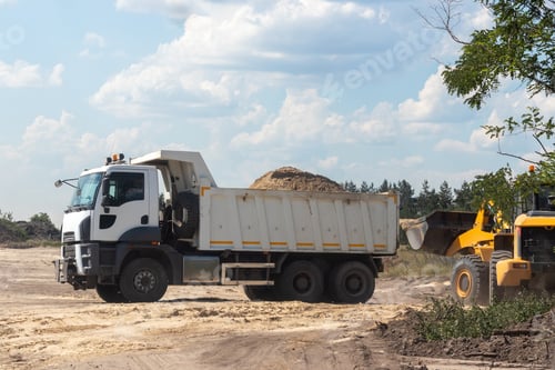 Preview: Dump truck with a bunch of land in the back and excavator at the construction site