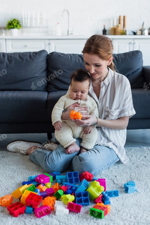 Preview: woman sitting on floor with infant african american girl near multicolored building blocks