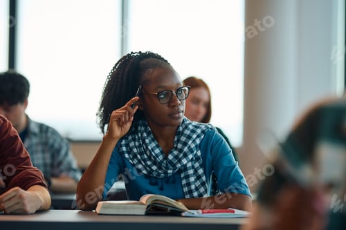 Preview: Pensive black female student learning at college classroom and looking away.