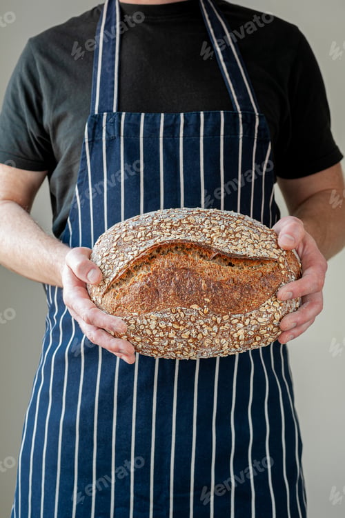 Preview: Close-up at bakers hands holding a loaf of bread in front of him.