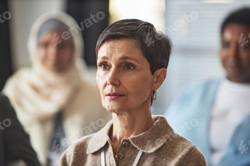 Preview: Middle aged brunette woman in casualwear listening to speaker report