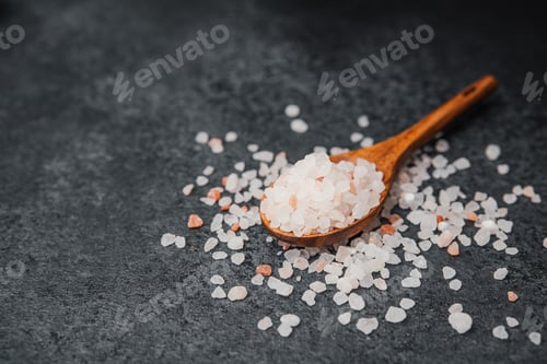 Preview: Wooden spoon filled with pink himalayan salt on textured black surface
