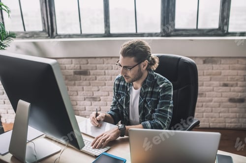 Preview: Young bearded man in eyeglasses making notes