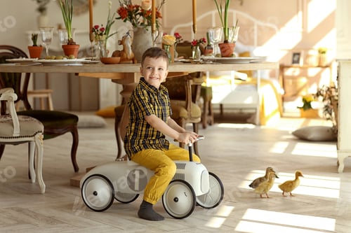 Preview: little boy on a toy car and ducklings on the background of the Easter table