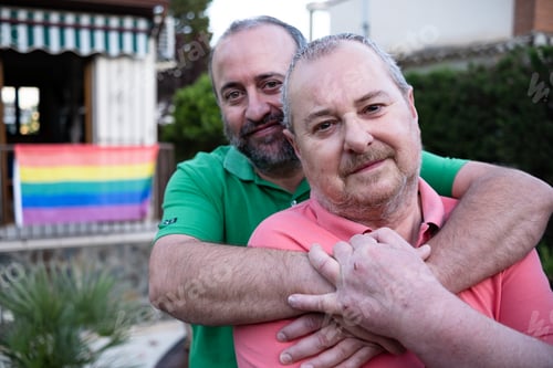 Preview: Gay couple hugging in yard with with LGBT flag on background
