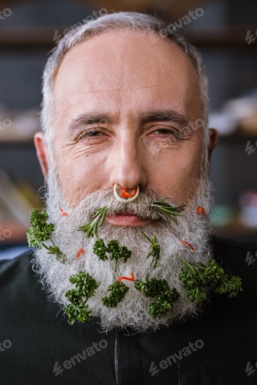 Preview: Close-up portrait of senior man with greens in beard smiling at camera