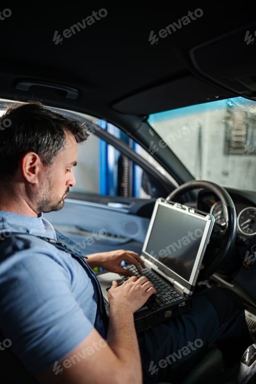 Preview: Car mechanic using laptop for diagnostics inside vehicle in auto repair shop