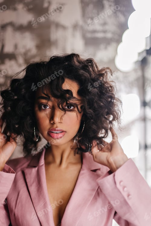 Preview: Elegant mixed race lady in pink jacket looking at camera. Front view of attractive female model wit