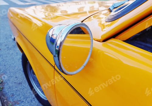 Preview: Close-up cropped image of side view mirror on a vintage yellow car.