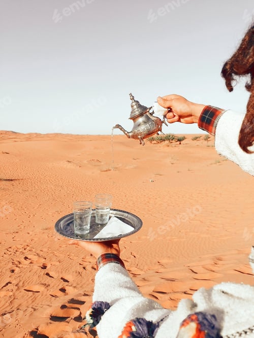 Preview: Hand pouring tea into a glass during Ramadan tea time in background of the Sahara desert in Morocco
