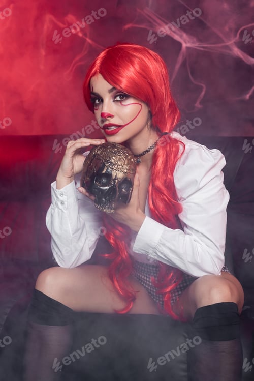 Preview: redhead woman in clown makeup holding golden skull in fog on dark background with spiderweb