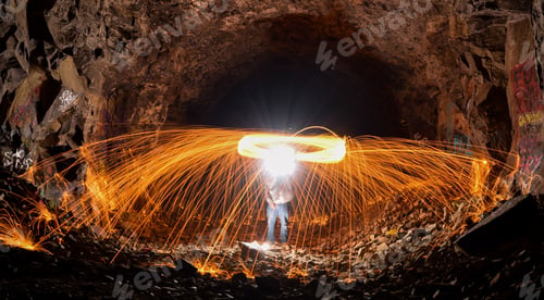 Preview: Long exposure shot of a person rotating a burning steel wool in a cave