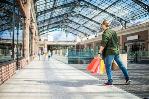 Preview: back view of man with shopping bags in hands looking for family in shopping center