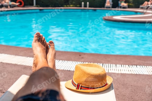 Preview: The legs of a man relaxing on a deck chair overlooking the water, sunbathing by the pool wearing
