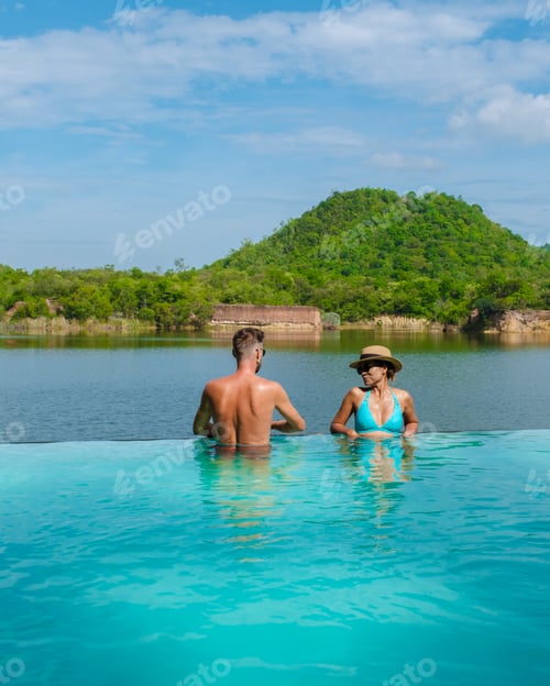 Preview: couple on the edge of a swimming pool in Thailand looking out over the lake and green mountain